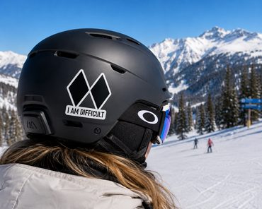 A close-up of a person wearing a matte black ski helmet with a white 'I AM DIFFICULT' sticker